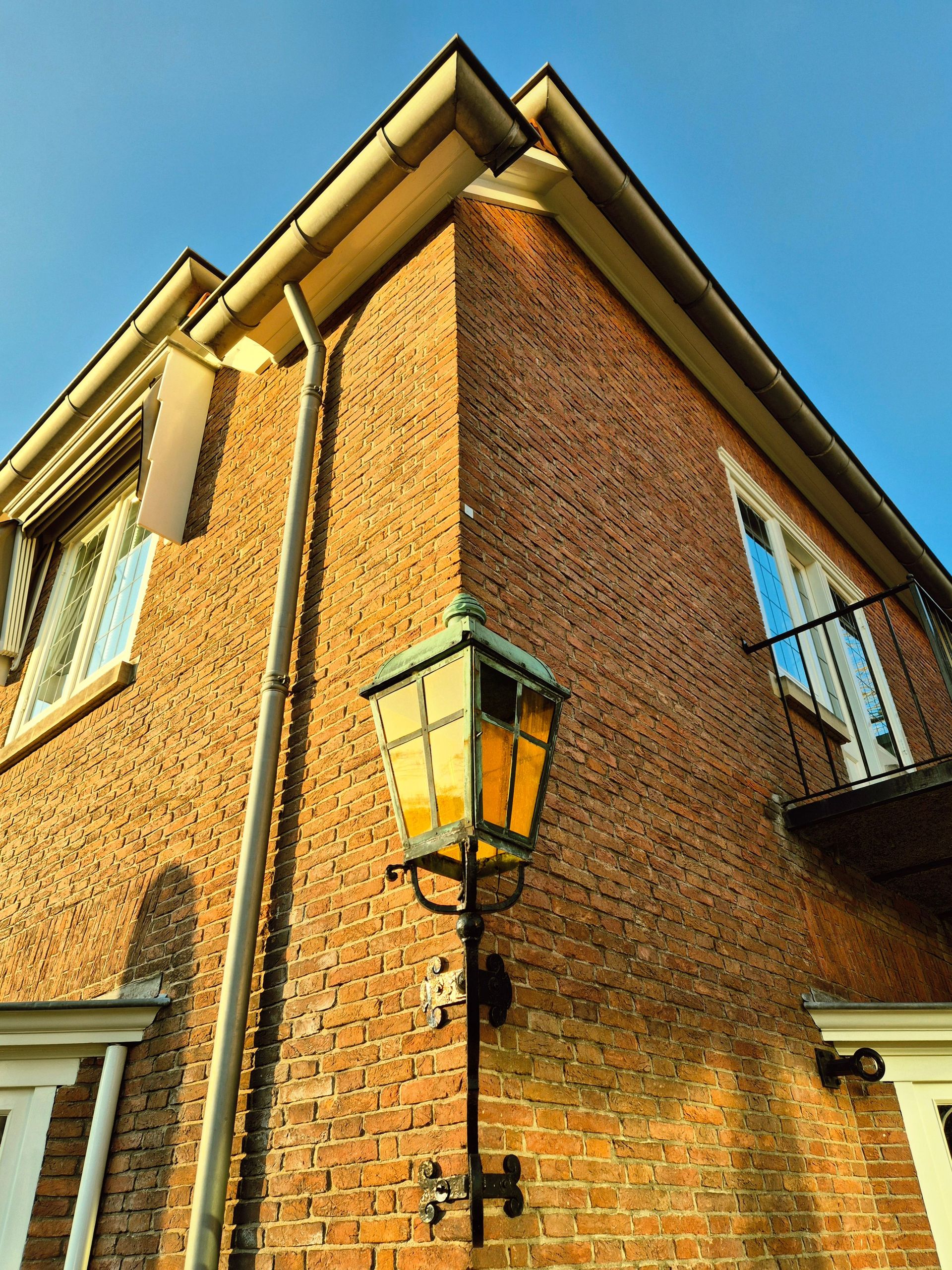 Corner view of a brick house with a vintage lantern under clear skies.